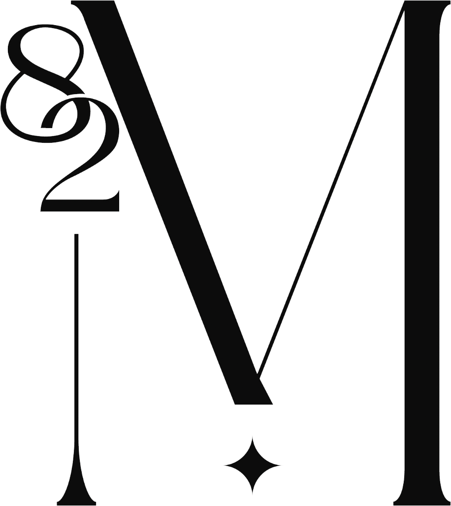 Elegant black serif letter M with intertwined ampersand, elongated thin strokes and small star ornament on white background