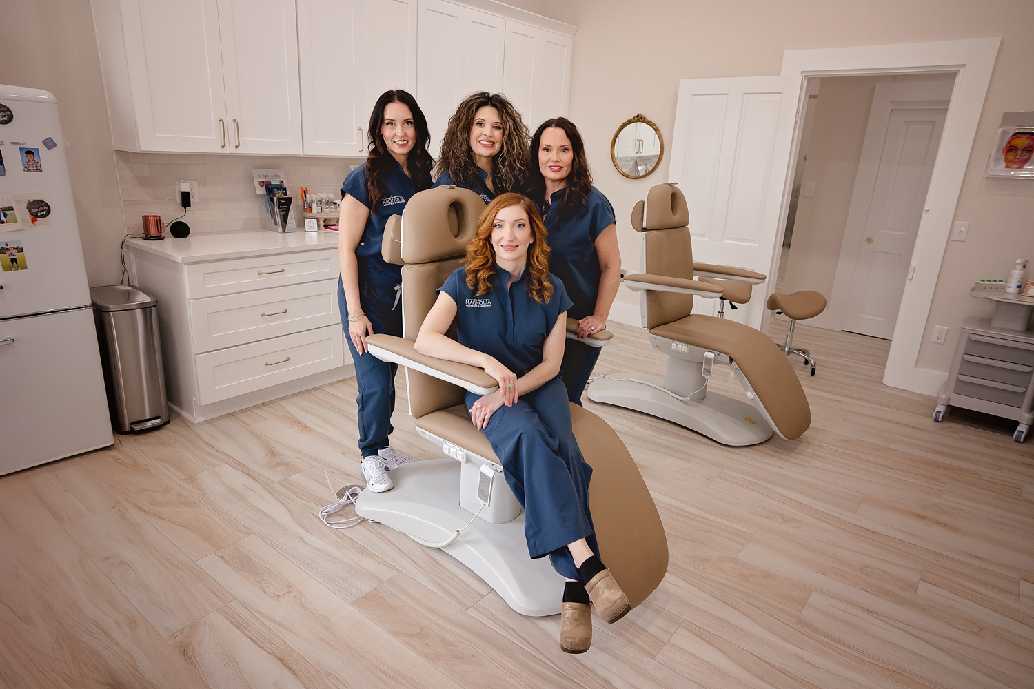 Dental clinic team of four women in navy scrubs posing around beige patient chairs in a bright modern treatment room