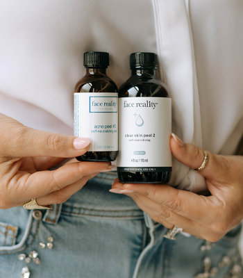 a person holding two Face Reality skincare bottles: Clear Skin Peel 2 and Acne Peel Kit in brown glass packaging