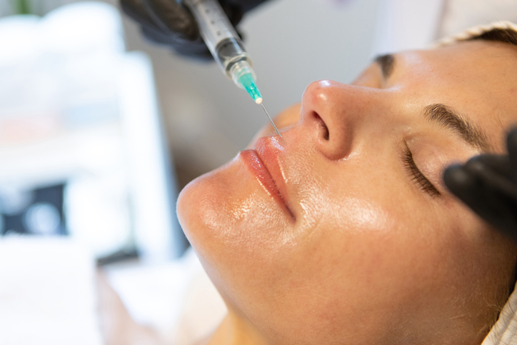 Woman receiving dermal lip filler injection at cosmetic clinic, close-up of lips and face.