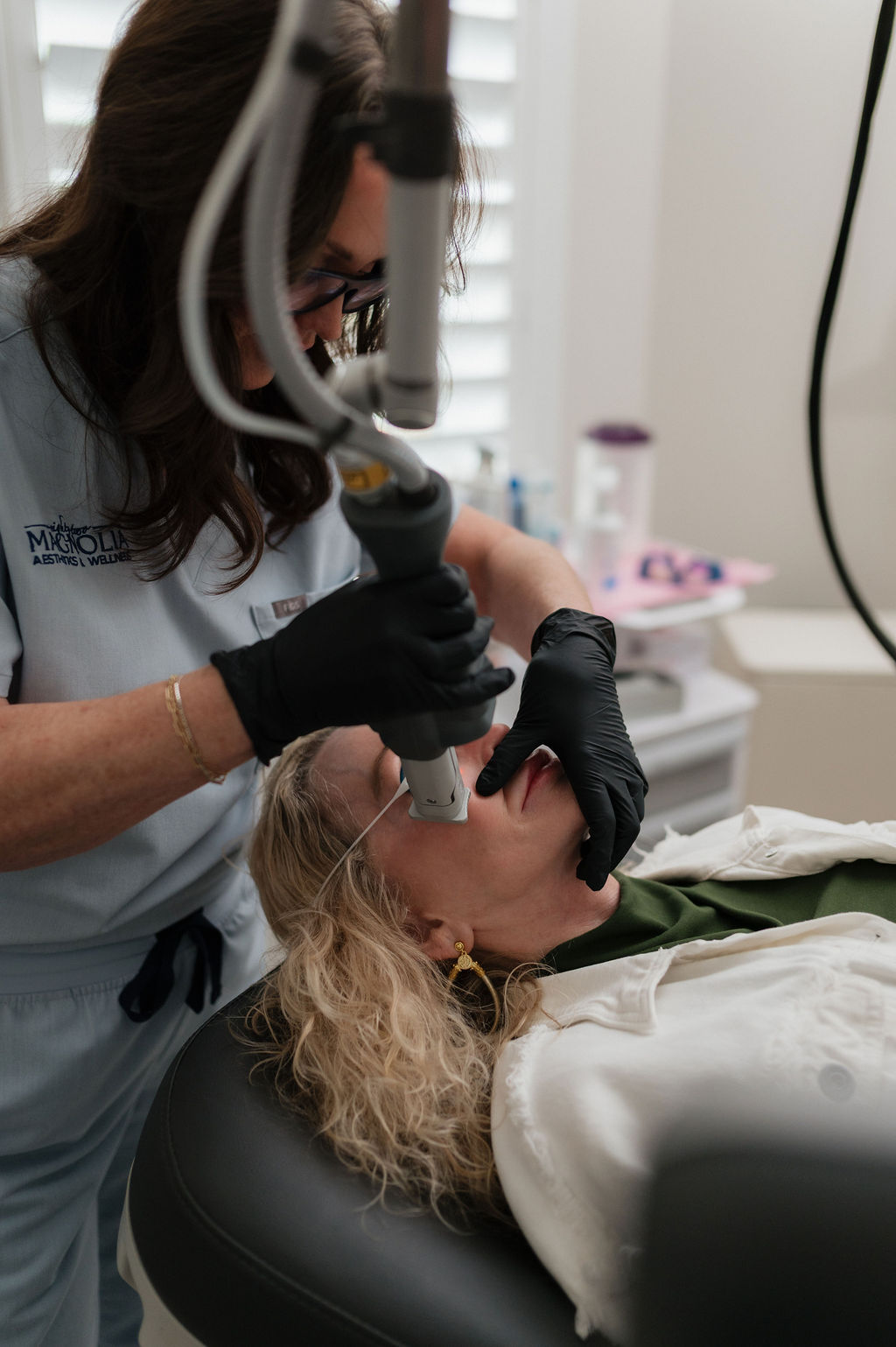 A woman reclines as a clinician in gloves performs a laser skin treatment on her lower face