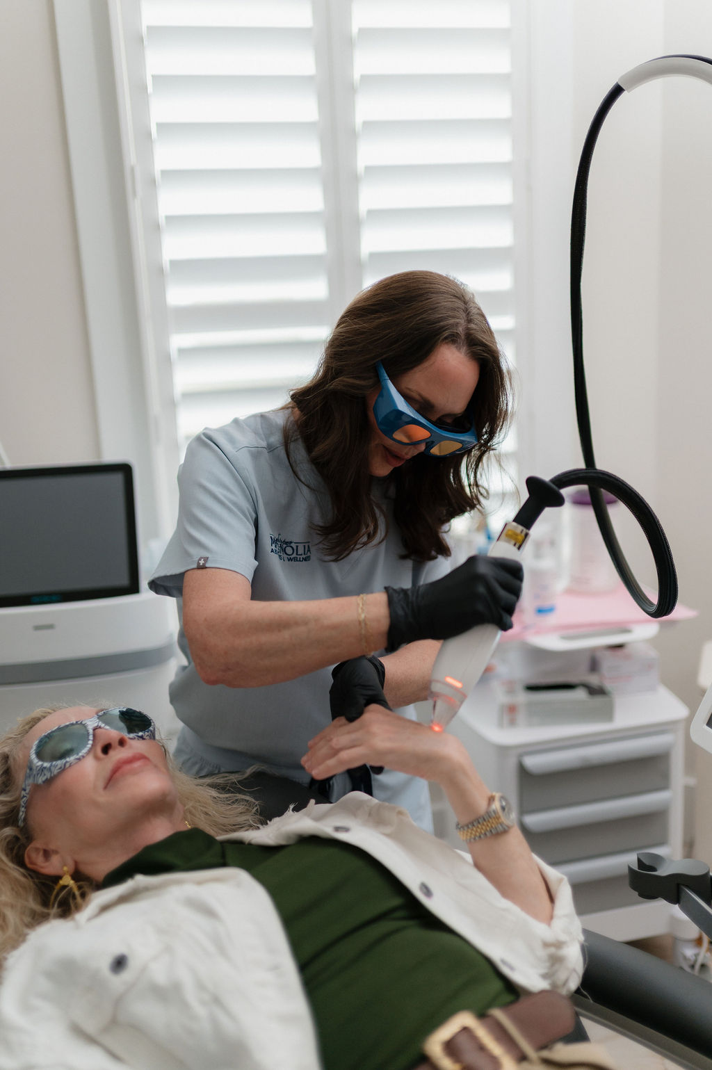 A woman receiving laser hand treatment from a clinician wearing protective goggles and gloves in a medical spa
