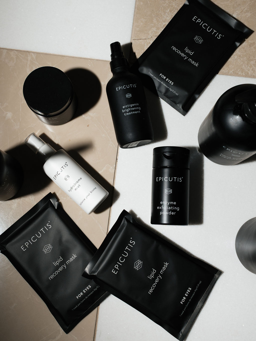 Flatlay of black EPICUTIS skincare: lipid recovery masks, enzyme exfoliating powder, hydrobione mist on marble.