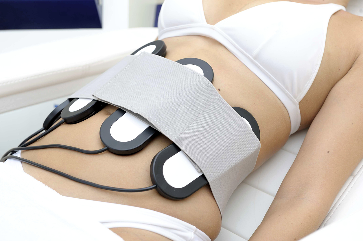 A woman receiving abdominal electrostimulation with multiple EMS pads and belt for body contouring