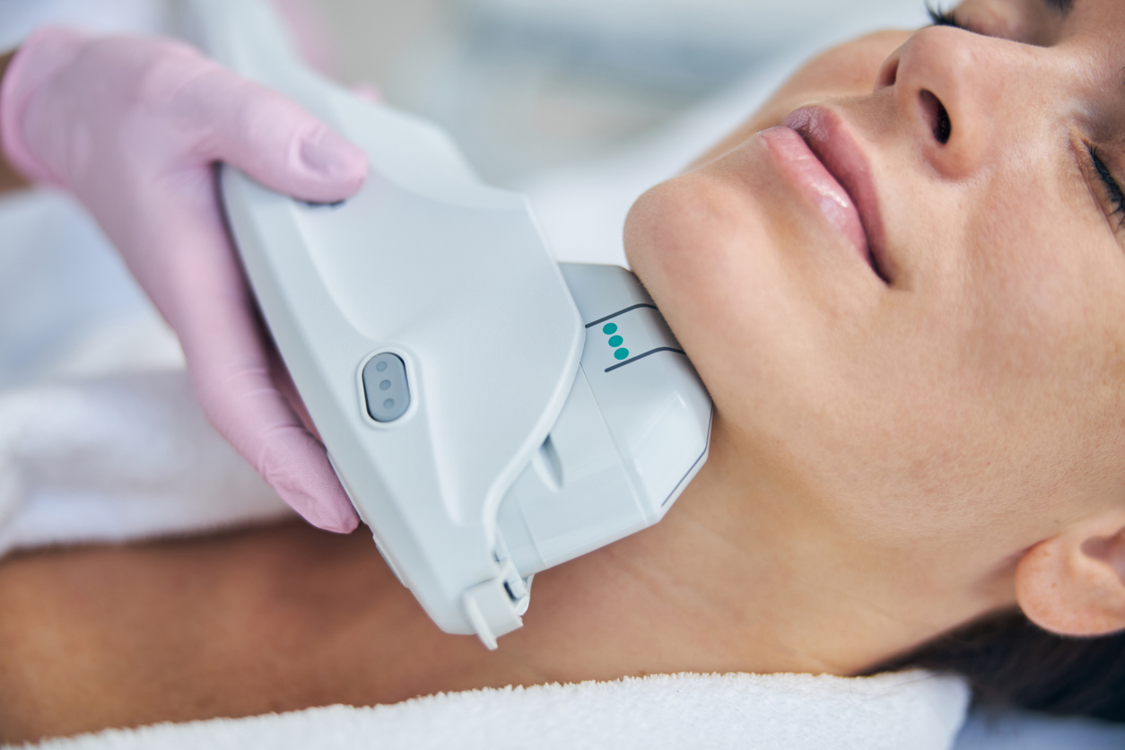 A woman receiving non-invasive ultrasound skin tightening treatment on neck and jawline