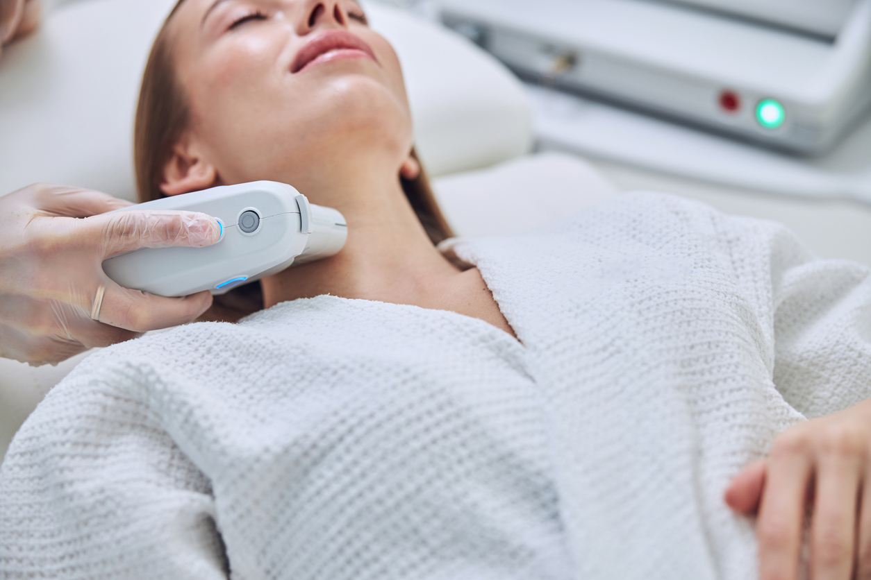 A woman receiving cosmetic laser skin tightening treatment on her neck in a clinic setting