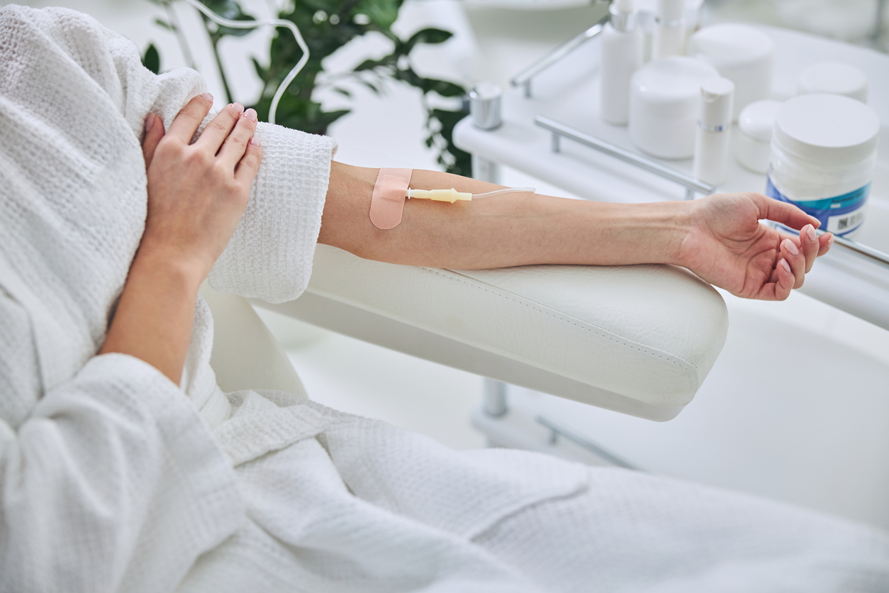 A woman in a white robe receiving intravenous therapy through a catheter in her arm at a wellness clinic.