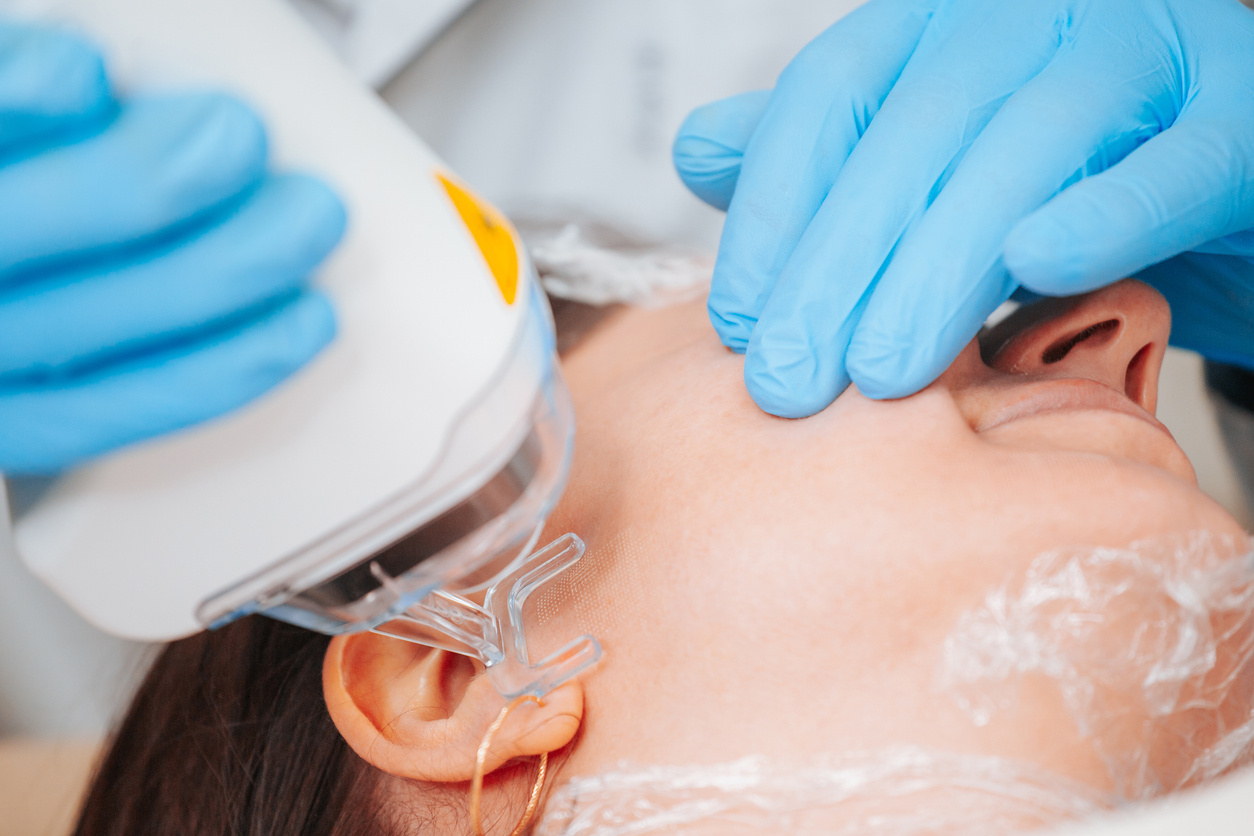Close-up of a woman receiving a non-invasive facial treatment with a handheld aesthetic device and blue-gloved clinician