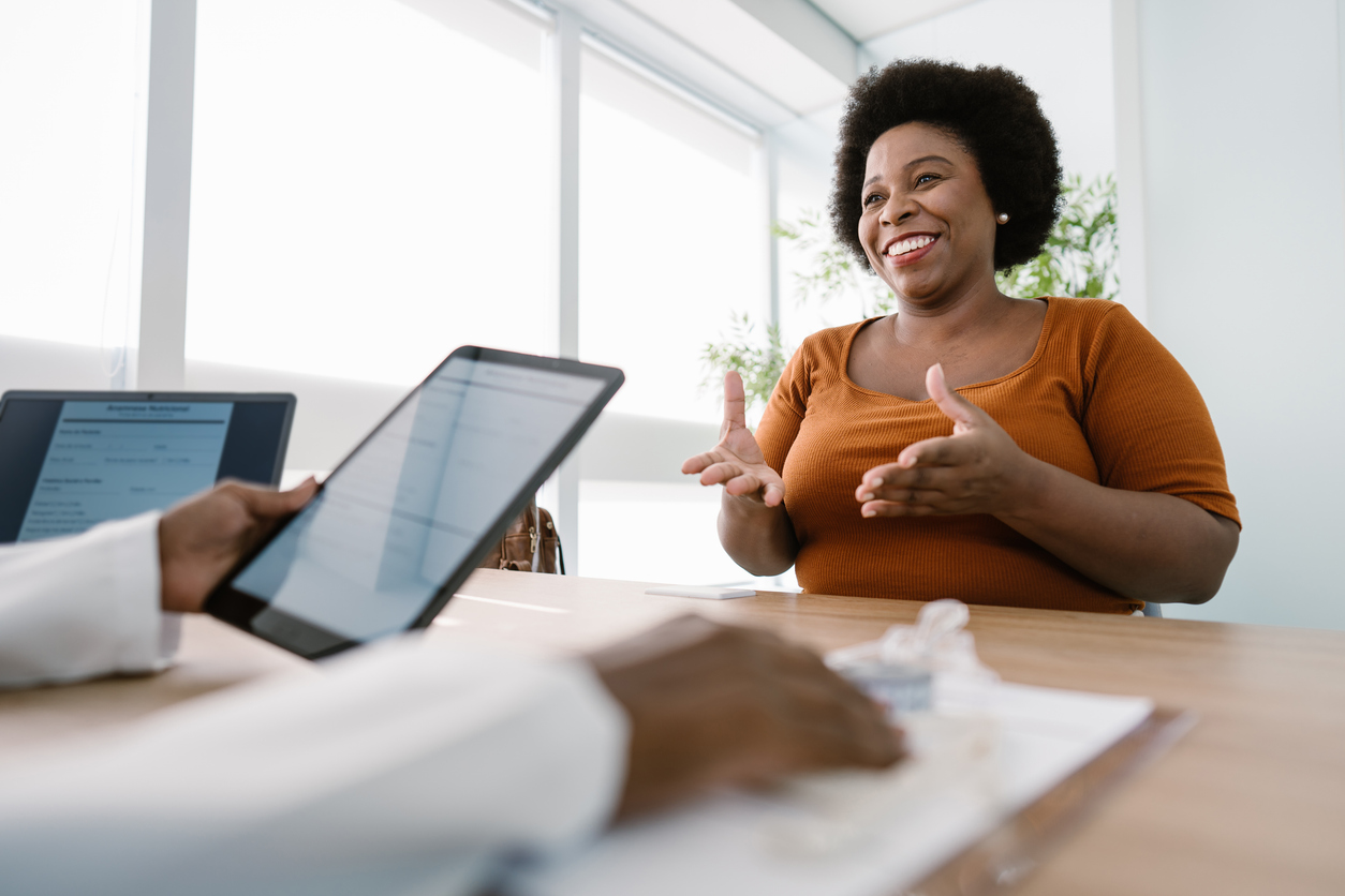 Smiling woman gesturing during a consultation as a professional reviews a tablet across the desk