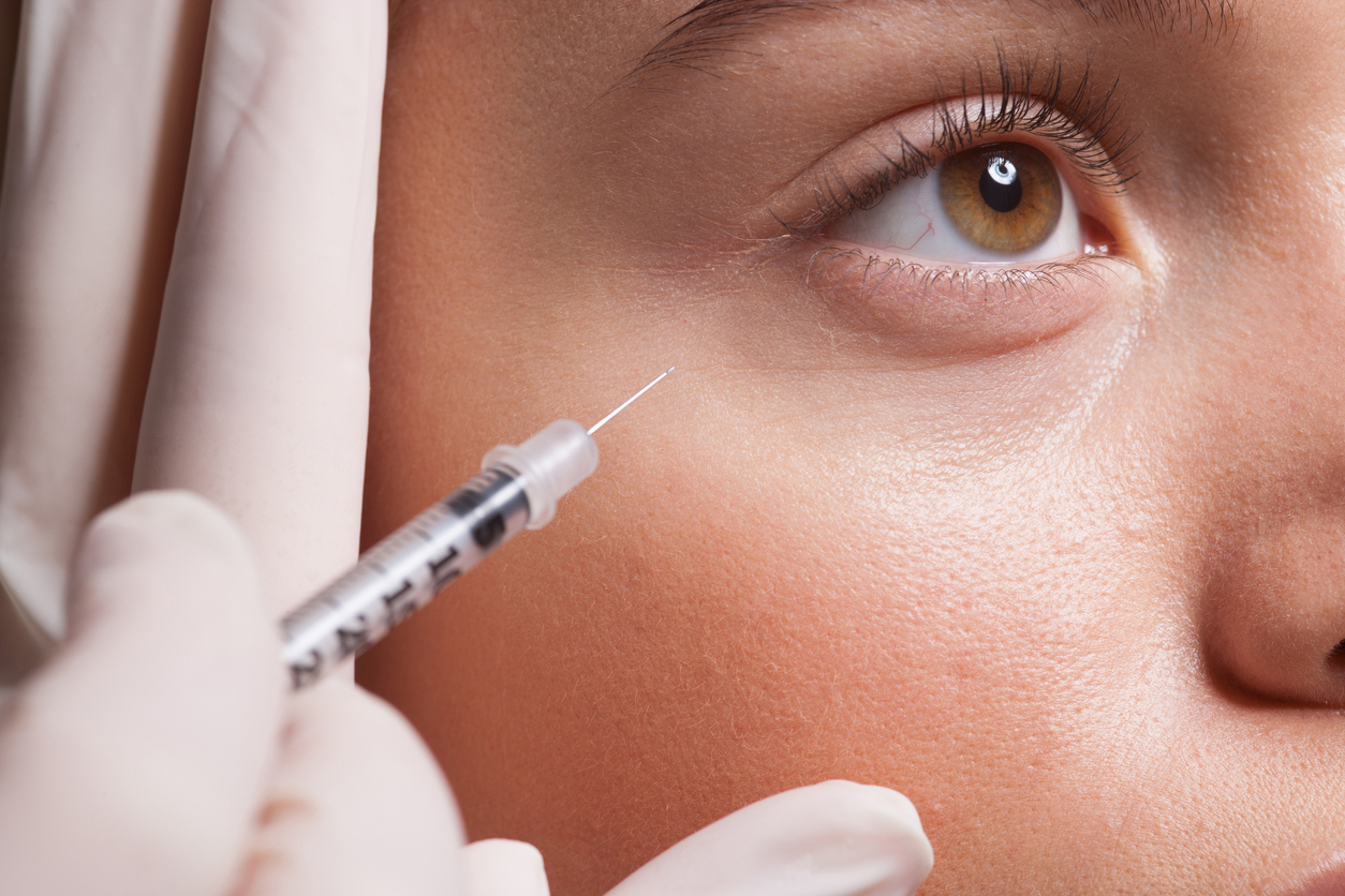 Close-up of a woman receiving a cosmetic under-eye injection with syringe for dermal filler treatment
