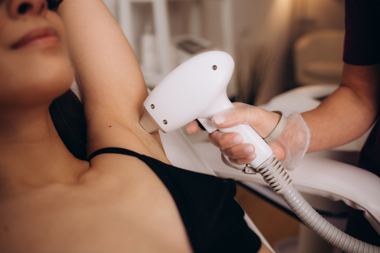 A woman receiving laser hair removal on underarm in clinic, technician holding handheld laser device.