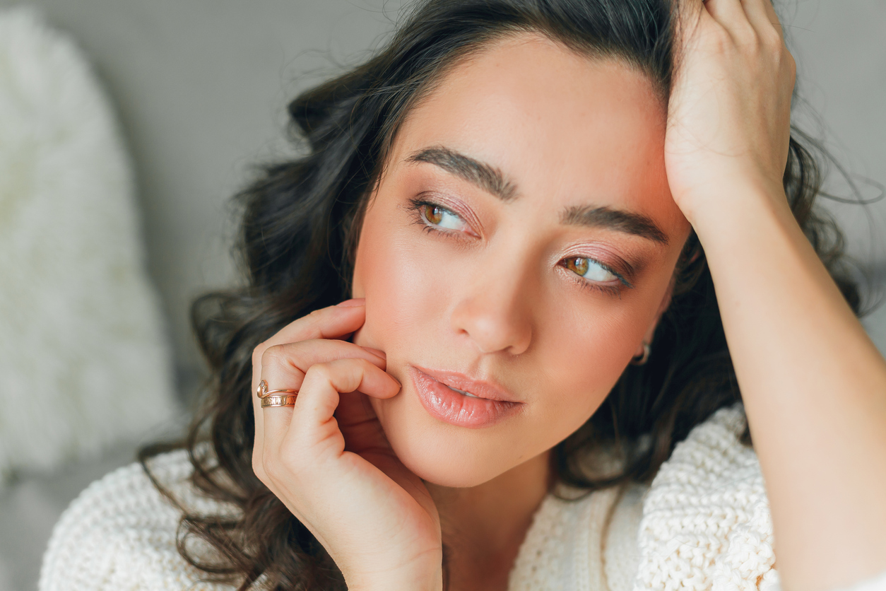 Close-up portrait of a thoughtful woman with natural makeup, brown eyes, wearing rings and cozy knit sweater in soft light