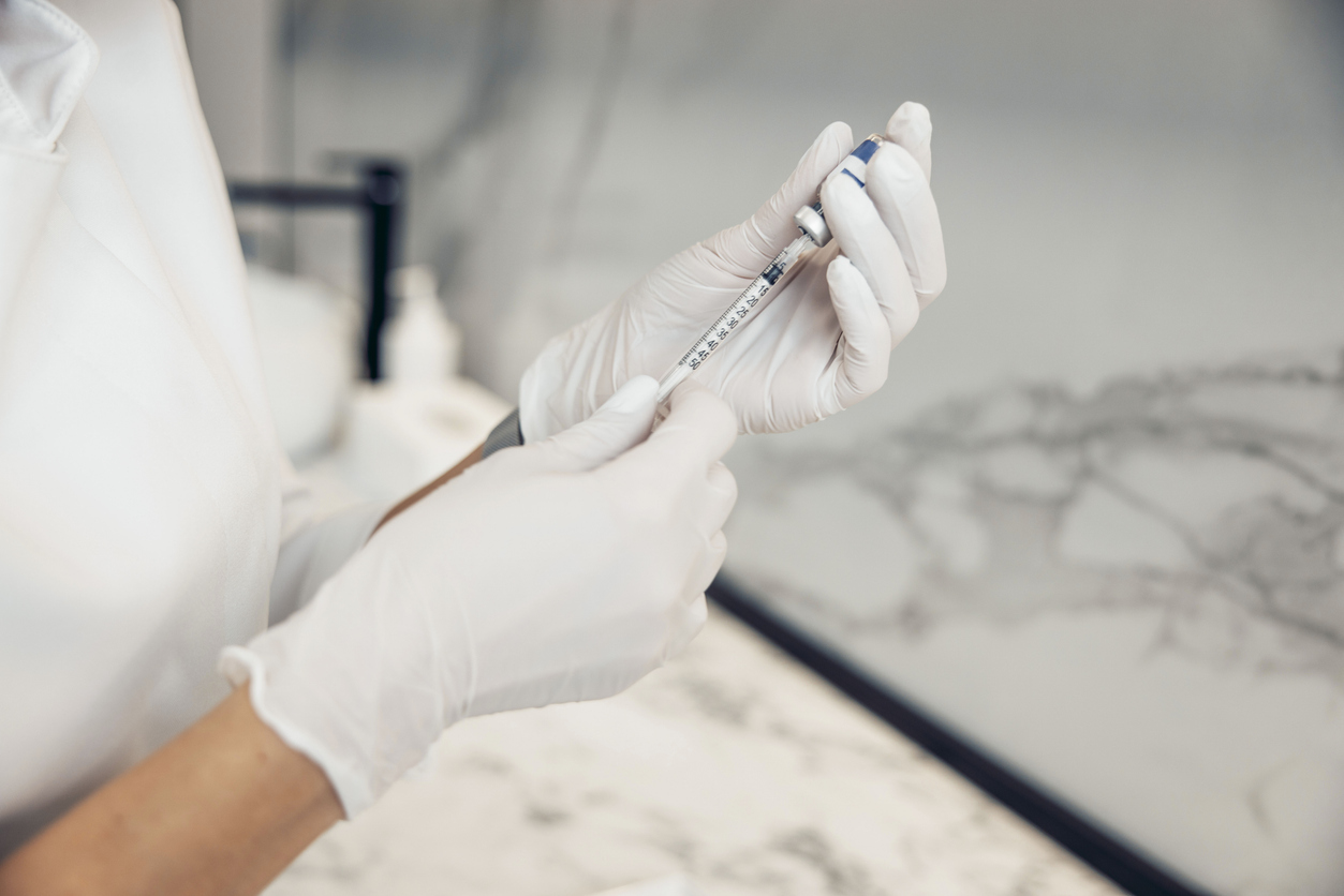 A person in medical gloves drawing vaccine into a syringe from a vial
