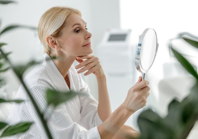 Smiling pretty woman using mirror in spa center