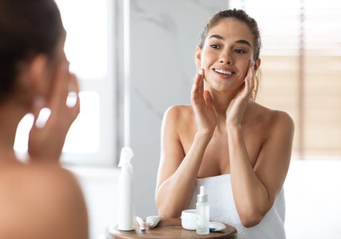 Happy Woman Touching Face Caring For Skin Standing In Bathroom